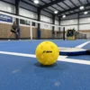 Balle de pickleball indoor X-ace 26 trous sur le parquet bleu d'un gymnase
