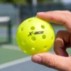 Balle de pickleball outdoor X-ace 40 trous tenue à la main sur un terrain extérieur