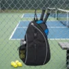 Sac sling pickleball noir accroché au grillage, 2 pagaies rangées